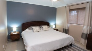 A neatly made bed with a striped rug, two bedside tables with lamps, and a ceiling fan.