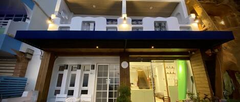 A two-story building with a balcony, a covered entrance, and a small outdoor seating area with a table and chairs.