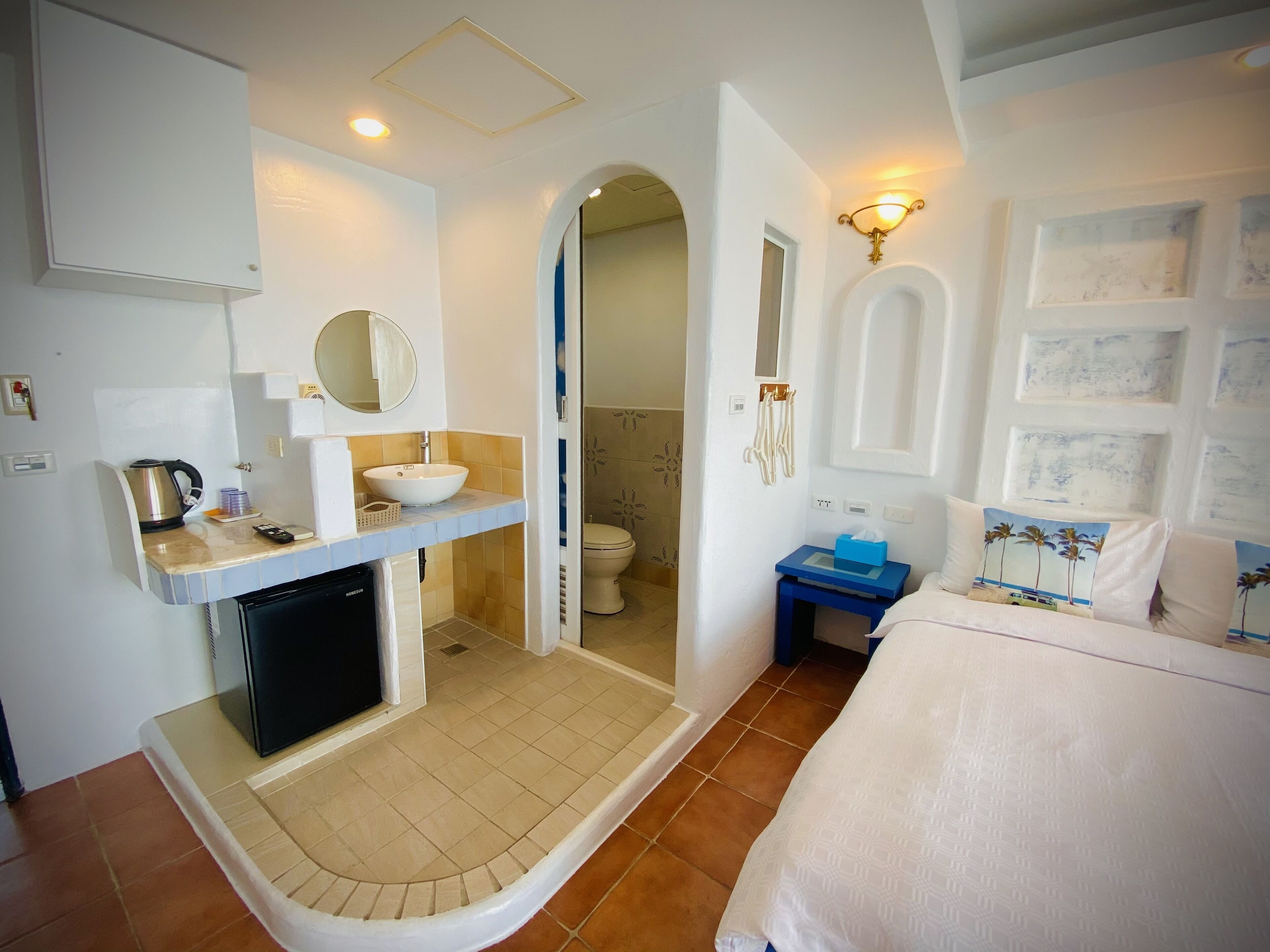 Un baño con lavamanos, espejo e inodoro. Cuenta con una zona de ducha, bañera y un pequeño taburete con una toalla y una caja.