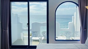 A bedroom with a large sliding glass door leading to a balcony with white chairs and a view of the sea. - Seya Inn (Hengchun)