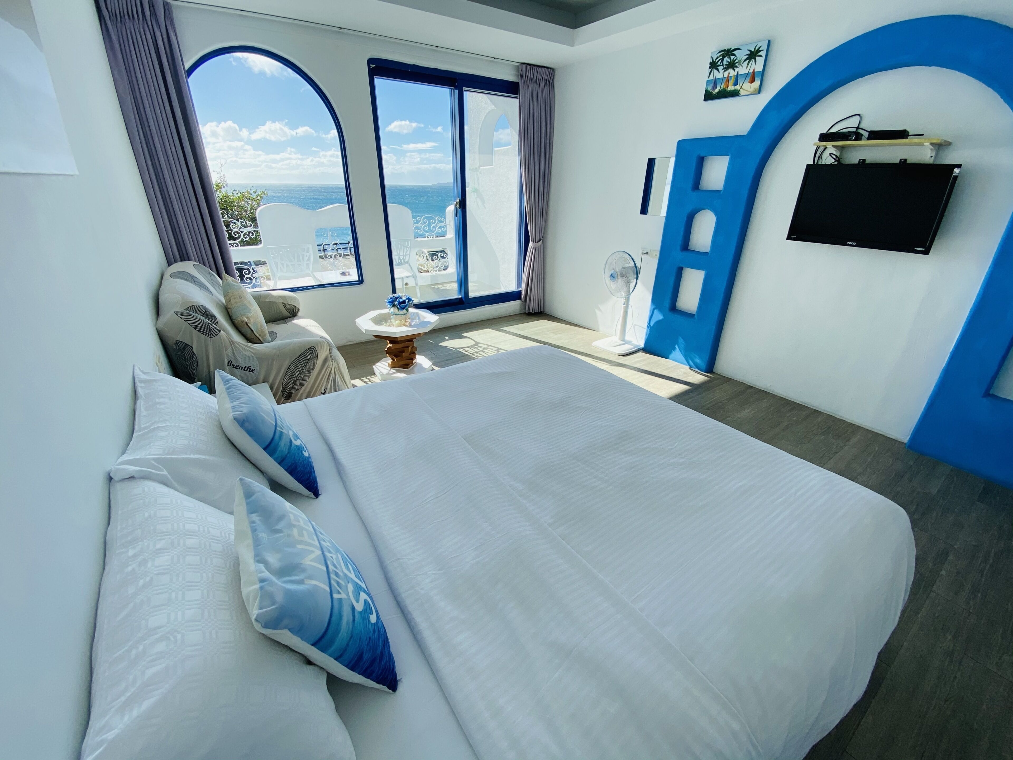 A hotel room with a large bed, a view of the sea, a balcony, and a blue accent wall.