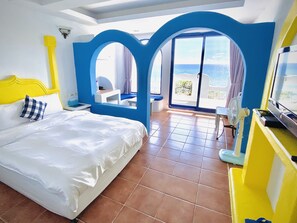 A hotel room with a bed, a desk, a chair, a TV, and a balcony with a view of the sea.