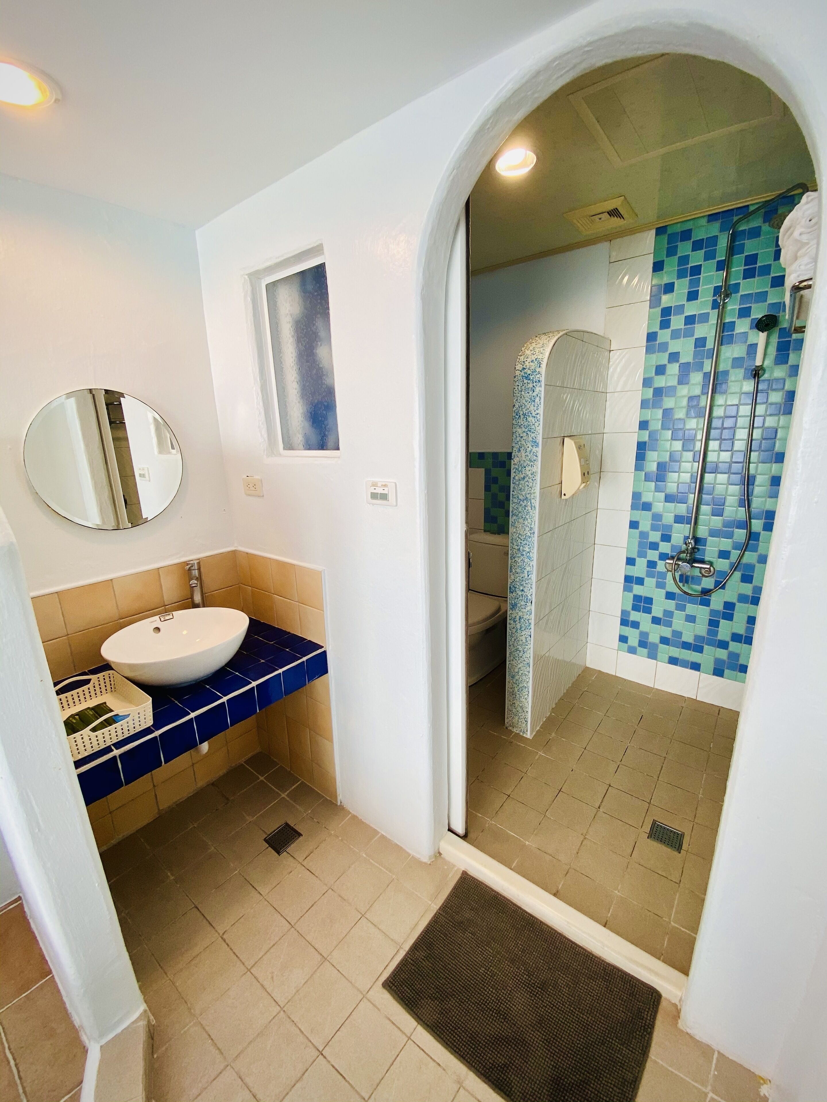 A bathroom with a white sink, blue tiles, a shower with a blue mosaic wall, and a mirror on the wall.