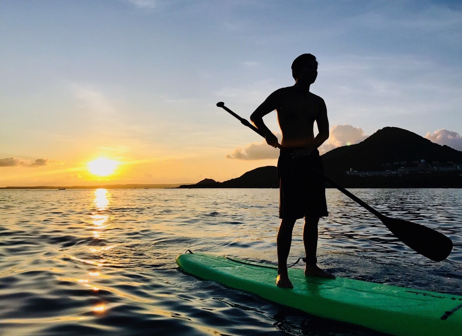 Una persona haciendo paddleboard en aguas tranquilas durante el atardecer, con montañas al fondo.