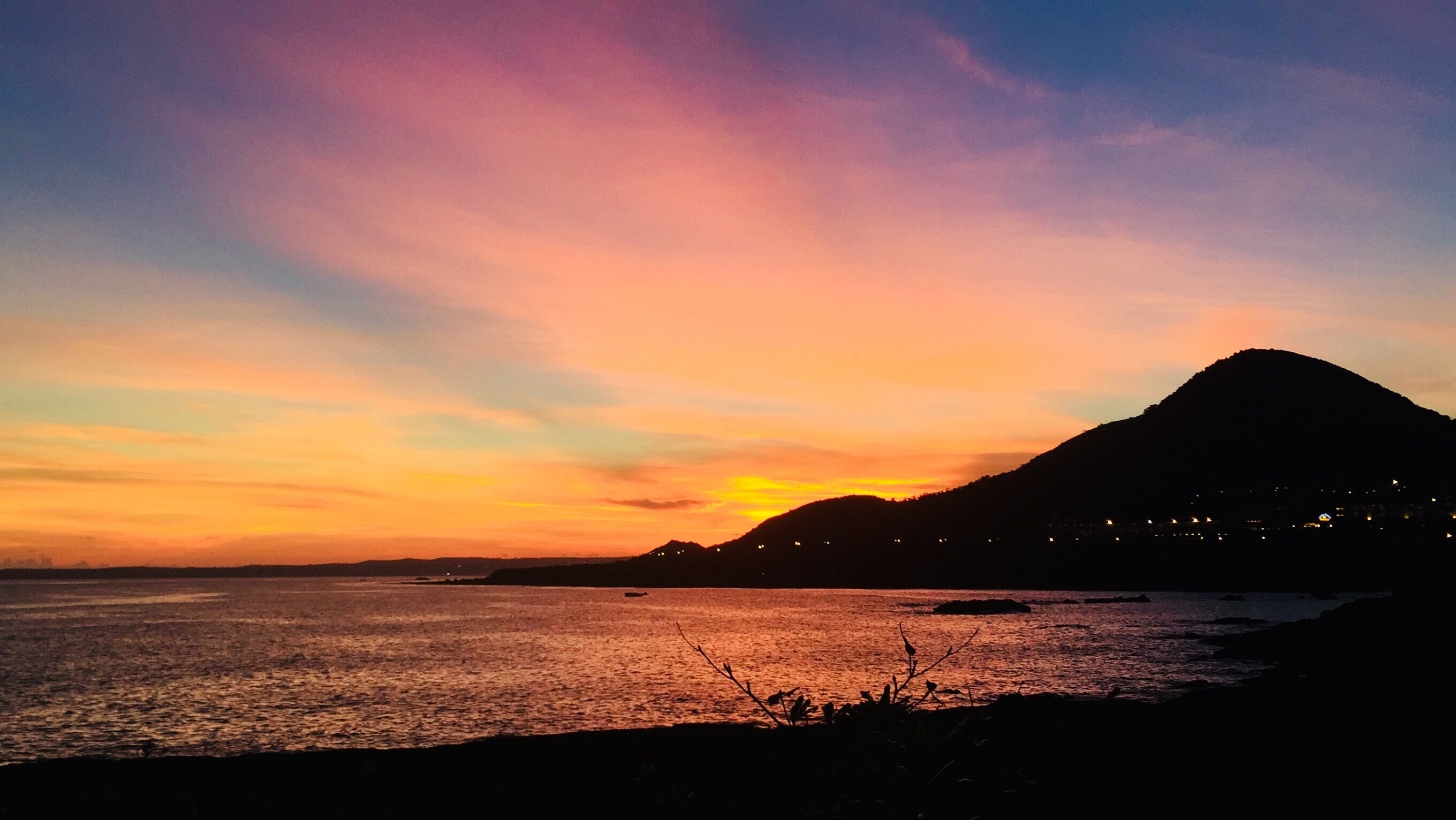 A sunset over a coastal landscape with a mountain in the background.