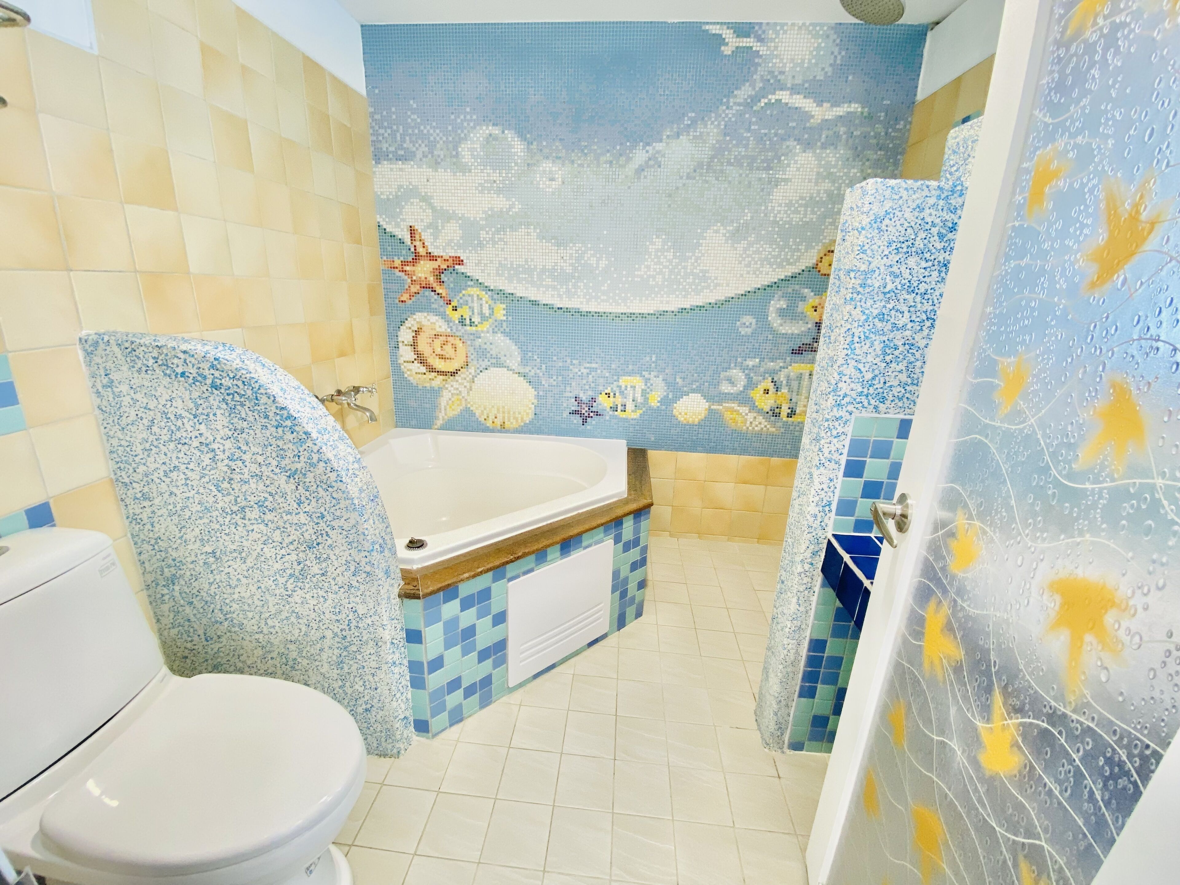 A bathroom with a mosaic wall, a bathtub, and a toilet.