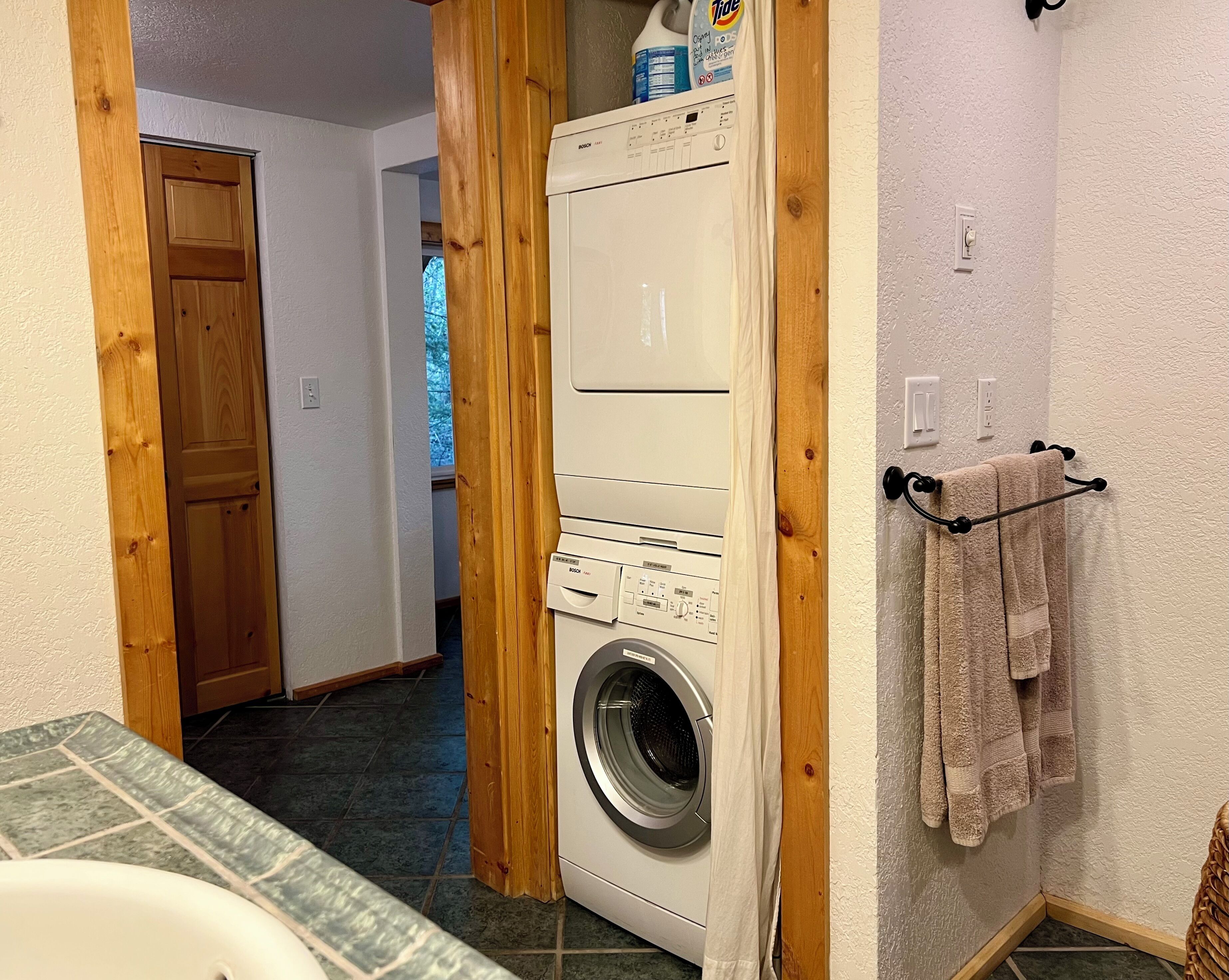 A laundry room with a Bosch washing machine, wooden door, and a towel rack.