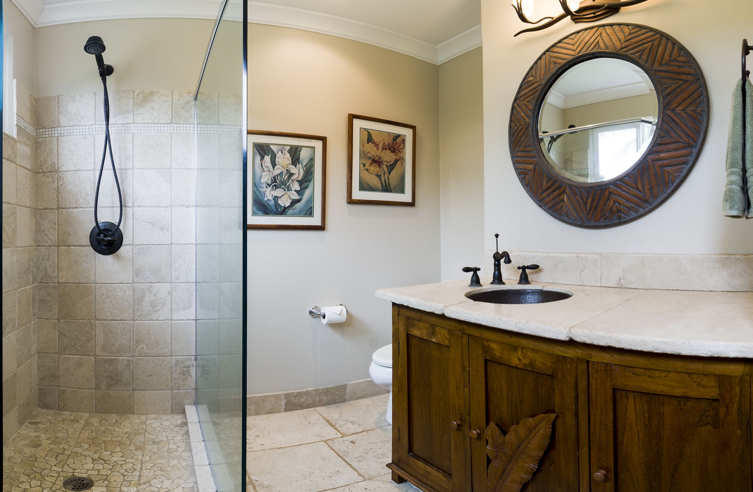 Een badkamer met douche, toilet, wastafel en twee lijstwerken met bloemen op de muur.