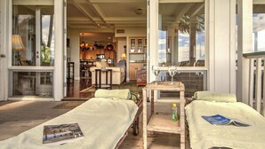 Une chambre avec deux lits, une petite table sur laquelle se trouvent une bouteille et un magazine, et une vue sur la cuisine et le salon grâce à des portes ouvertes.