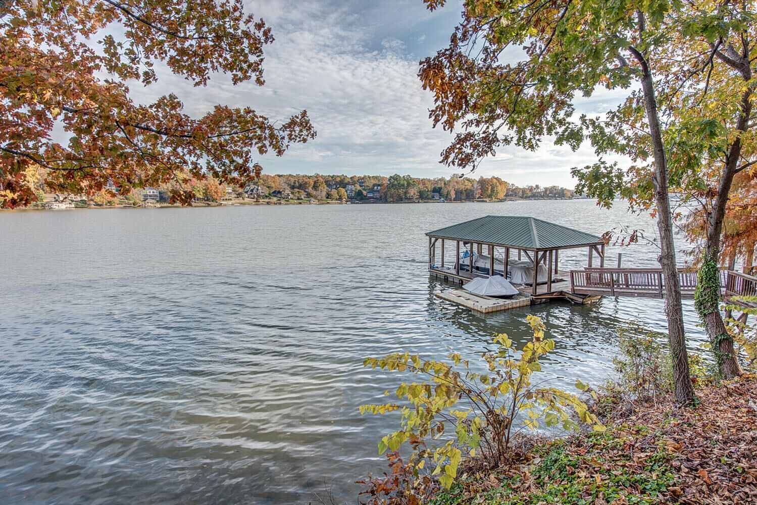 Ein Laubenhaus am Seeufer mit überdachter Veranda, umgeben von Herbstlaub und einem ruhigen See.