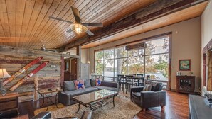 A spacious living area with a wooden ceiling, large windows offering a view of the outdoors, a fireplace, and a ski rack. - Firefly • Lakefront Estate • Dock + Beach + Kayaks (Belmont)