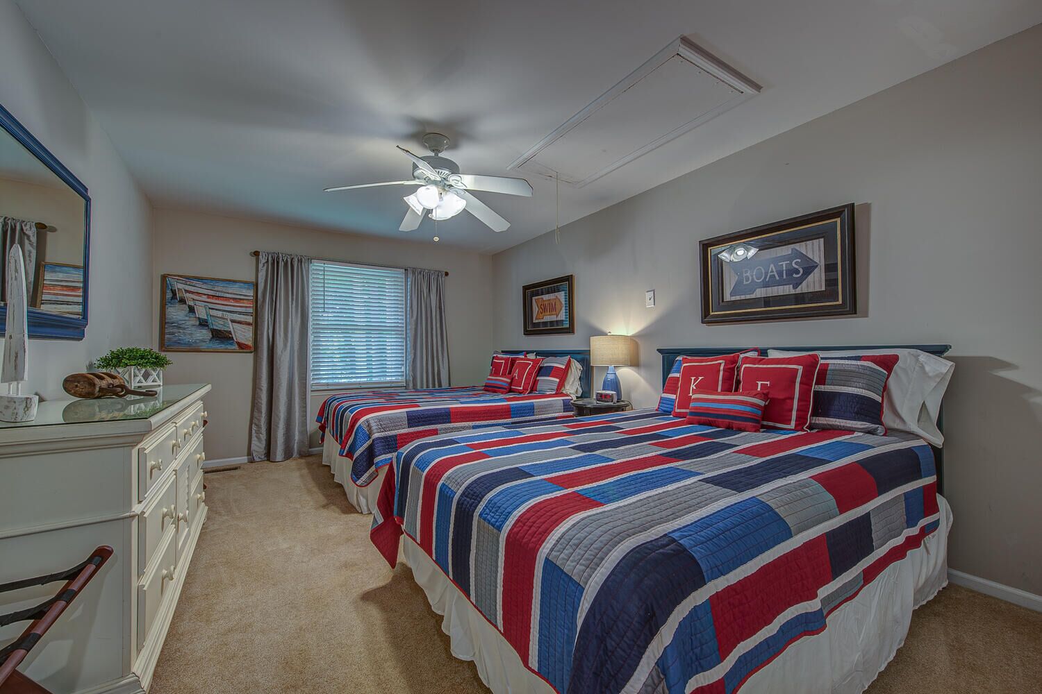 A bedroom with two beds, a ceiling fan, a dresser, and a window with curtains.