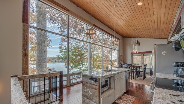 A spacious kitchen with large windows, a wooden ceiling, and a view of a lake. - Firefly • Lakefront Estate • Dock + Beach + Kayaks (Belmont)
