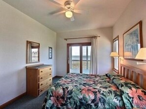Une chambre à coucher comprenant un lit, une commode, un ventilateur de plafond, une fenêtre avec vue et une porte donnant sur un balcon.