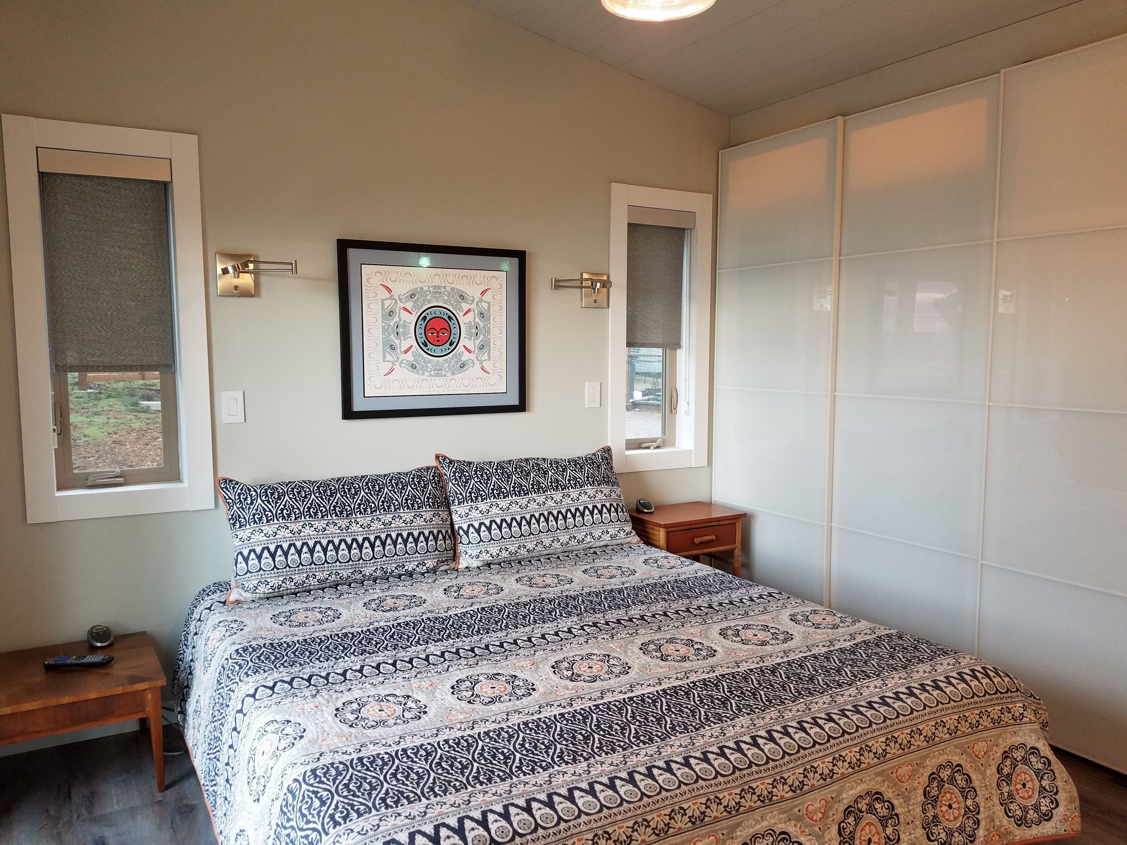 Une chambre à coucher avec une couvre-lit à motifs, une œuvre d’art encadrée accrochée au mur et une fenêtre donnant sur l’extérieur.