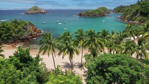 A coastal landscape with a beach, palm trees, and rocky outcrops. - Casita Jazmin Careyes - Beachfront Villa - Infinity Pool - Exoticdigs Collection (Careyes)