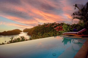 An infinity pool with a view of a coastal landscape and a sunset.
