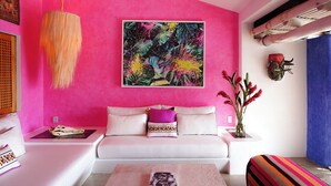 A room with a vibrant pink wall, a white sofa with colorful cushions, a hanging light fixture, and a painting above the sofa. - Casita Jazmin Careyes - Beachfront Villa - Infinity Pool - Exoticdigs Collection (Careyes)