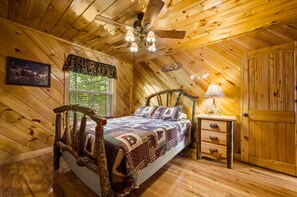 A wooden cabin bedroom with a bed, a nightstand, a lamp, and a door.