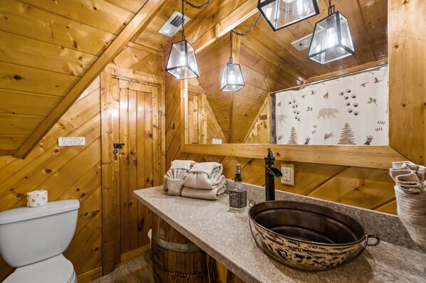 A wooden cabin bathroom with a toilet, sink, and hanging lights.