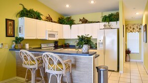 A kitchen with white cabinets, a microwave, a refrigerator, and two wicker bar stools. - 140+ Reviews, Steps to Beach, Magnificent Water Views, None Cleaner, None Nicer! (Indian Shores)