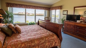 A bedroom with a large bed, a dresser, a television, and a view of a body of water through large windows. - 140+ Reviews, Steps to Beach, Magnificent Water Views, None Cleaner, None Nicer! (Indian Shores)