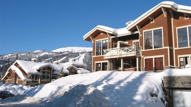 Un hotel grande de varios pisos, con un balcón destacado, rodeado de montañas nevadas y un cielo despejado.