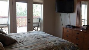 A bedroom with a bed, a dresser, a television mounted on the wall, and a sliding glass door leading to an outdoor area.
