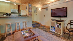 Ein gemütlicher Wohnbereich mit Küche, Holzboden, einem Flachbildfernseher und einem Bücherregal.