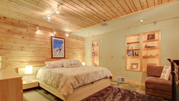 Ein Schlafzimmer mit Holzboden, einem Bett mit Kopfteil, einem Nachttisch, einem Lesesessel und integrierten Bücherregalen.