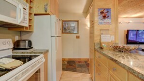 Eine kompakte Küche mit Mikrowelle, Toaster und Kühlschrank. An der Wand hängt ein Poster mit Skifahrern, und ein Fernseher ist dort montiert.