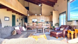 A spacious living area with a high ceiling, wooden ceiling beams, a dining area with a wooden table and chairs, and a kitchen with wooden cabinets. - LABOR DAY WEEKEND IS NOW AVAILABLE - escape the heat! (Flagstaff)