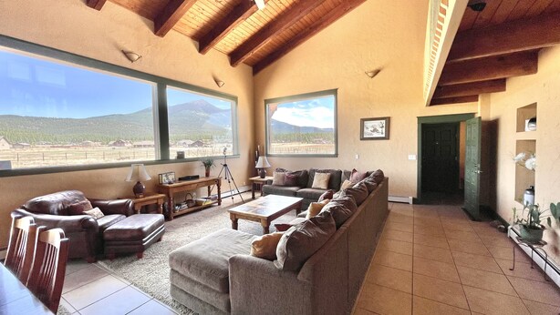 A spacious living room with a large window offering a mountain view, a cozy seating area with a sofa and chairs, and a wooden ceiling. - LABOR DAY WEEKEND IS NOW AVAILABLE - escape the heat! (Flagstaff)