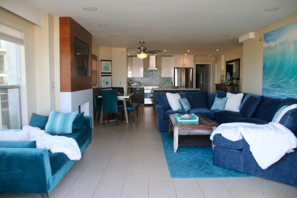 A modern living room with a sofa set, a coffee table, and a dining area in the background.