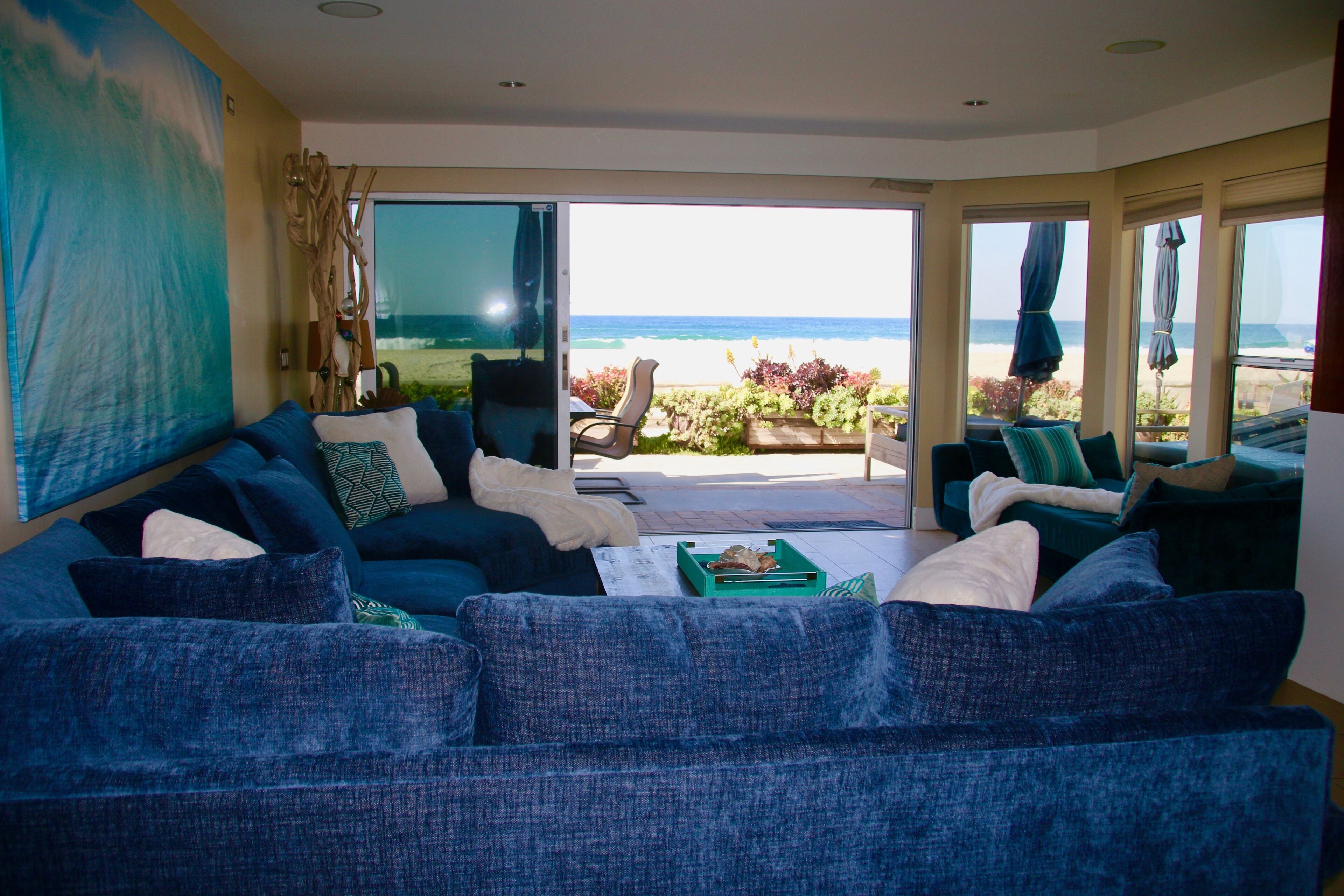 A living room with a large blue sofa, a coffee table, and a view of the beach through large windows.