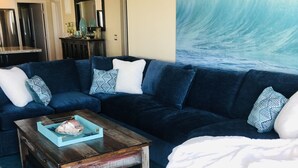 Un salón con un sofá de color azul oscuro, una mesa de centro de madera y una alfombra estampada en azul.