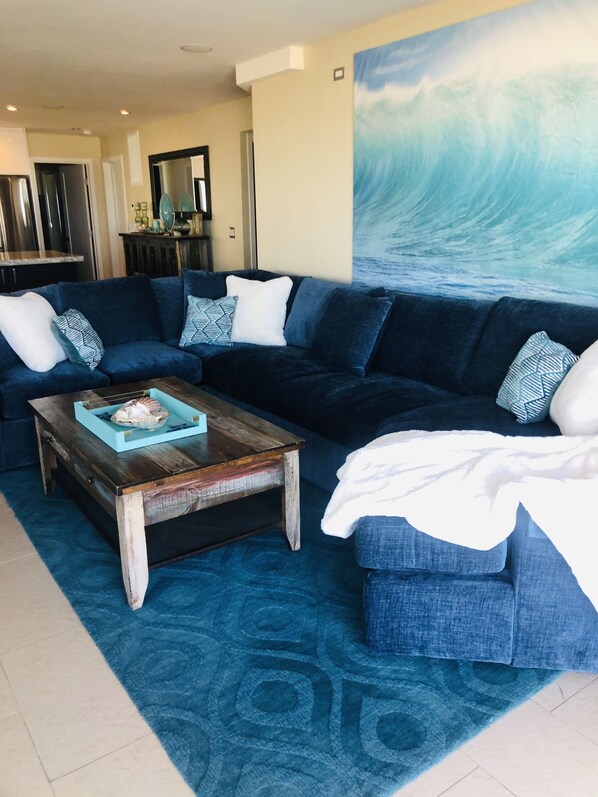 Un salón con un sofá de color azul oscuro, una mesa de centro de madera y una alfombra estampada en azul.