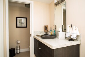 A modern bathroom with a large sink, dark cabinets, a mirror, and a toilet visible in the background.