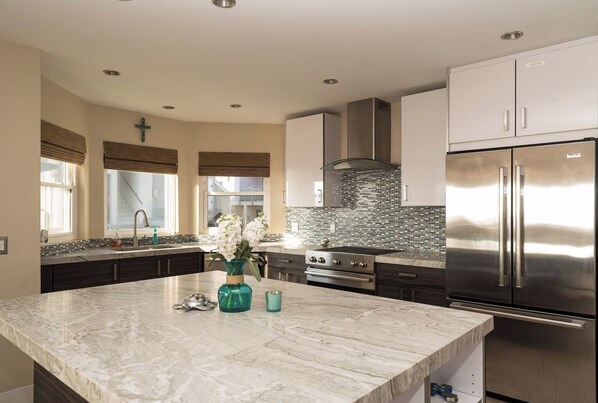 A modern kitchen with a marble island, stainless steel appliances, and a tiled backsplash.