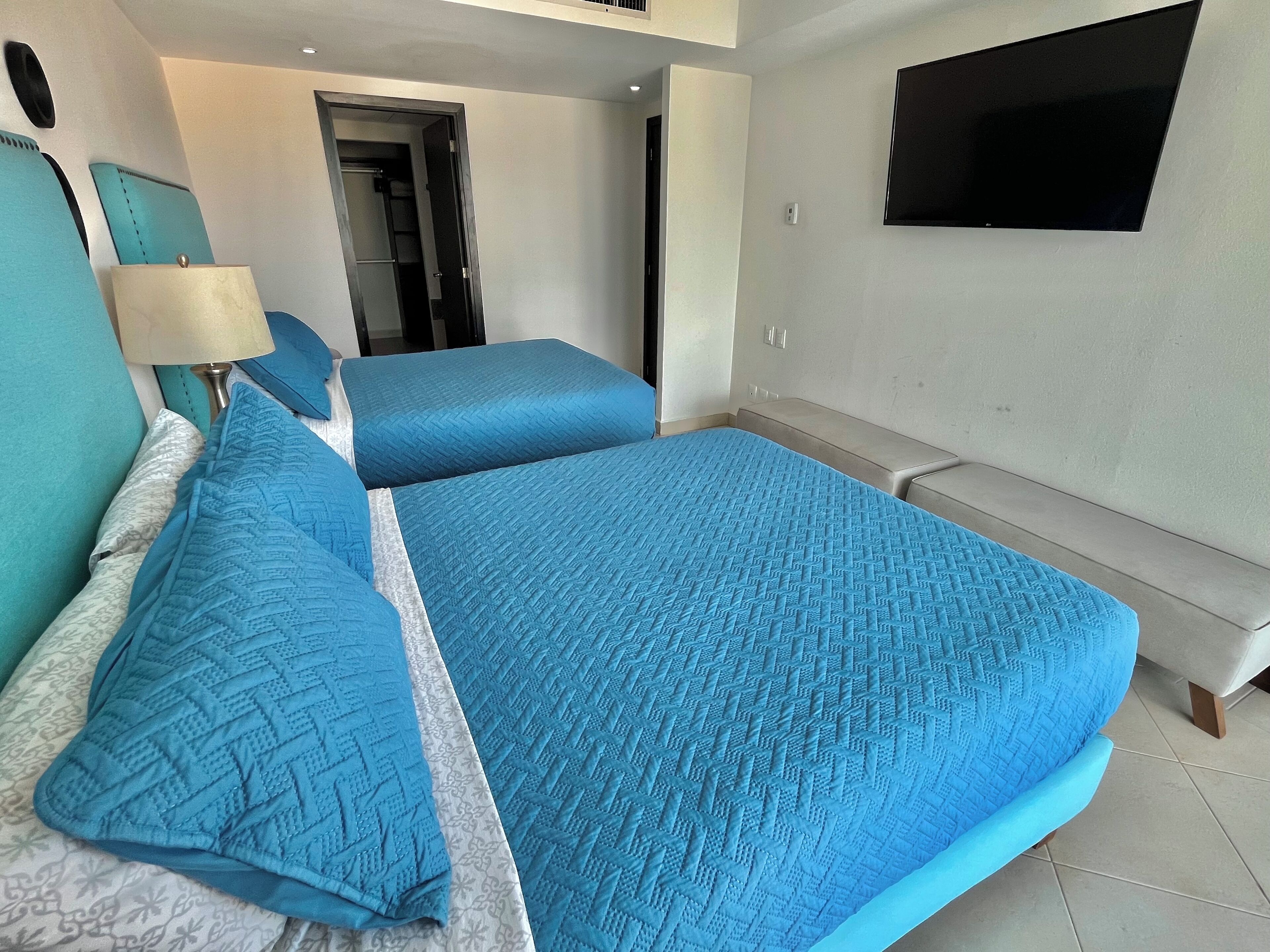 A hotel room with a large bed, a bench, a TV, and a door leading to a bathroom.