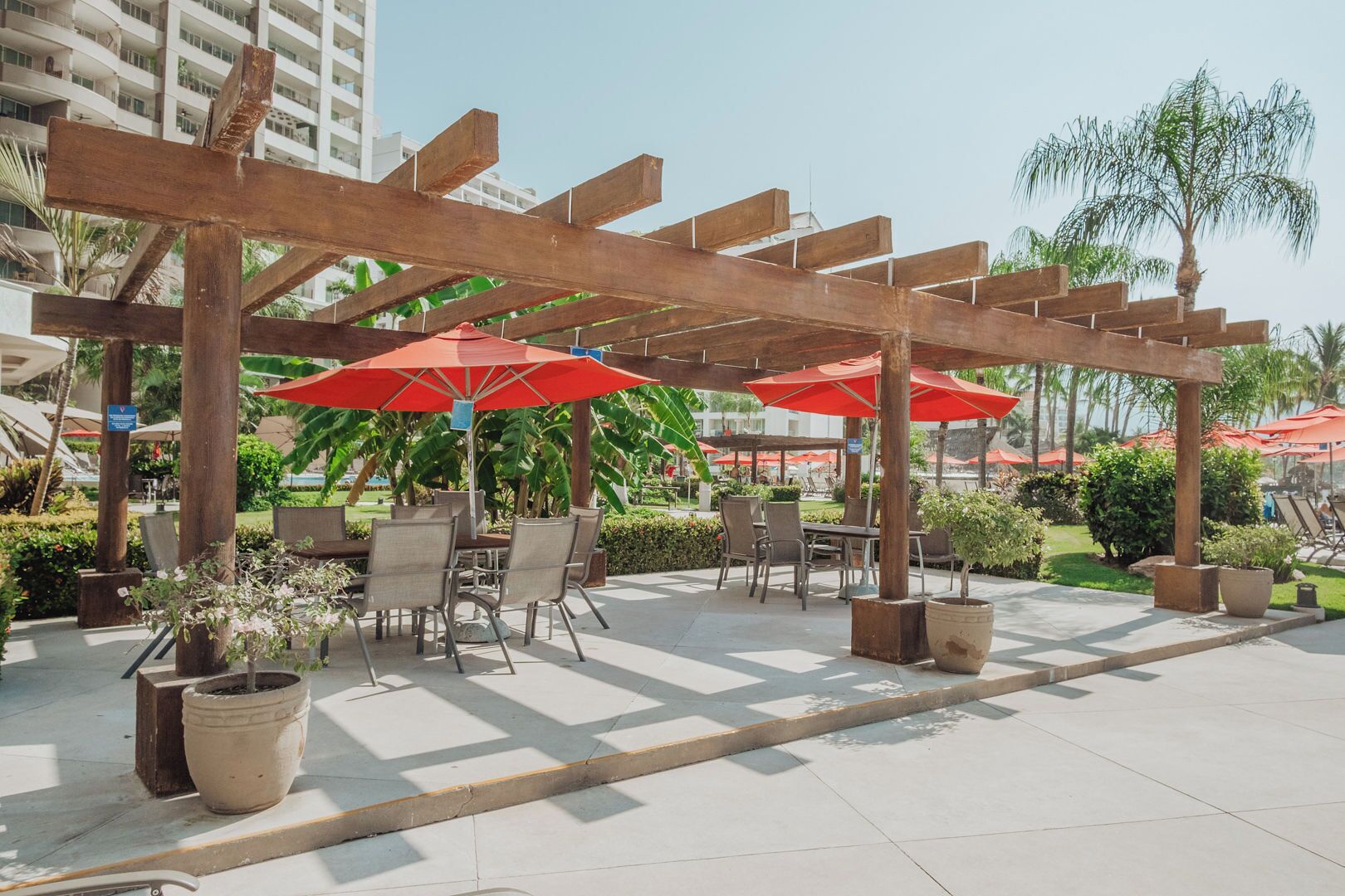 An outdoor patio area with wooden pergolas, red umbrellas, and outdoor seating.