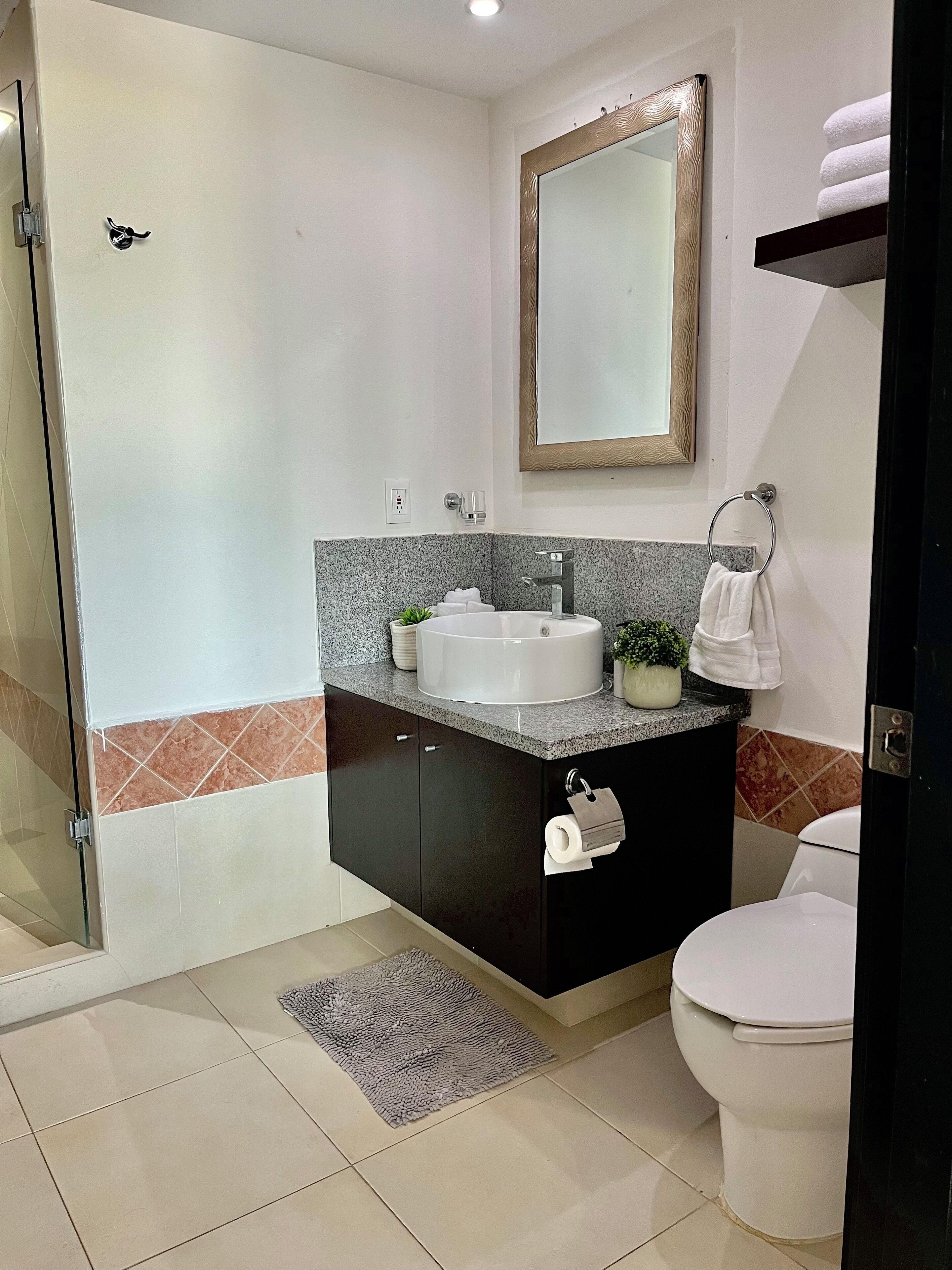 A modern bathroom with a white sink, black cabinets, a mirror, and a toilet.