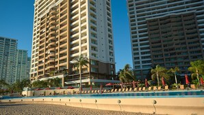 Un hotel con varios pisos, piscina y mobiliario exterior con sombrillas.