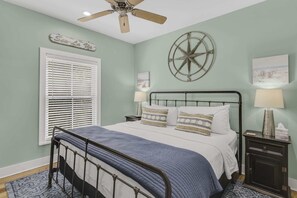 Ein Schlafzimmer mit einem Bett, einem Deckenventilator, einem Fenster mit Jalousien, einem an der Wand befestigten Kompass und einem Nachttisch mit einer Lampe.