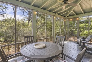 A covered outdoor patio with a round table and chairs, large windows, and a ceiling fan.