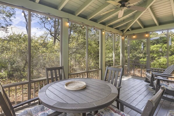 A covered outdoor patio with a round table and chairs, large windows, and a ceiling fan.