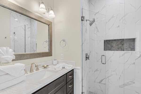 A bathroom with a marble vanity, a large mirror, a shower with a glass door, and a small stone accent wall.