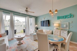 A room with a ceiling fan, a dining table with chairs, a TV mounted on the wall, and a word 'Beach' displayed on the wall.