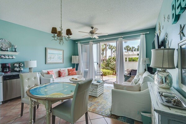 A room with a dining table, a sofa, a ceiling fan, and a view of the outdoors.