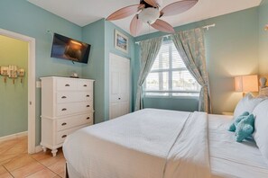 A bedroom with a bed, a dresser, a ceiling fan, a TV, and a window with curtains.